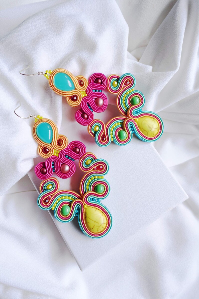 Pu&ograve; includere: Un paio di orecchini colorati con un design in turchese, giallo e verde. Gli orecchini sono realizzati con filo intrecciato e perline.