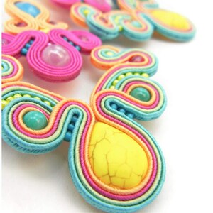 Pu&ograve; includere: Un paio di orecchini colorati fatti a mano con un motivo arcobaleno e pietre turchesi e gialle.