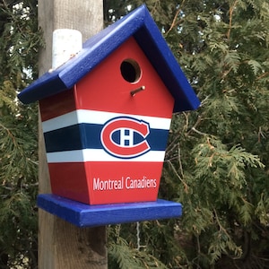 May include: A blue and red birdhouse with a Montreal Canadiens logo and the text "Montreal Canadiens". The birdhouse is mounted on a wooden post.