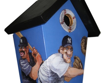 Puede incluir: Una casita de pájaros azul y negra con temática de béisbol. La parte delantera de la casita de pájaros presenta dos jugadores de béisbol de dibujos animados que llevan uniformes de los New York Yankees. Un jugador sostiene un bate y el otro un guante de béisbol. La casita de pájaros tiene una abertura redonda para que los pájaros entren.