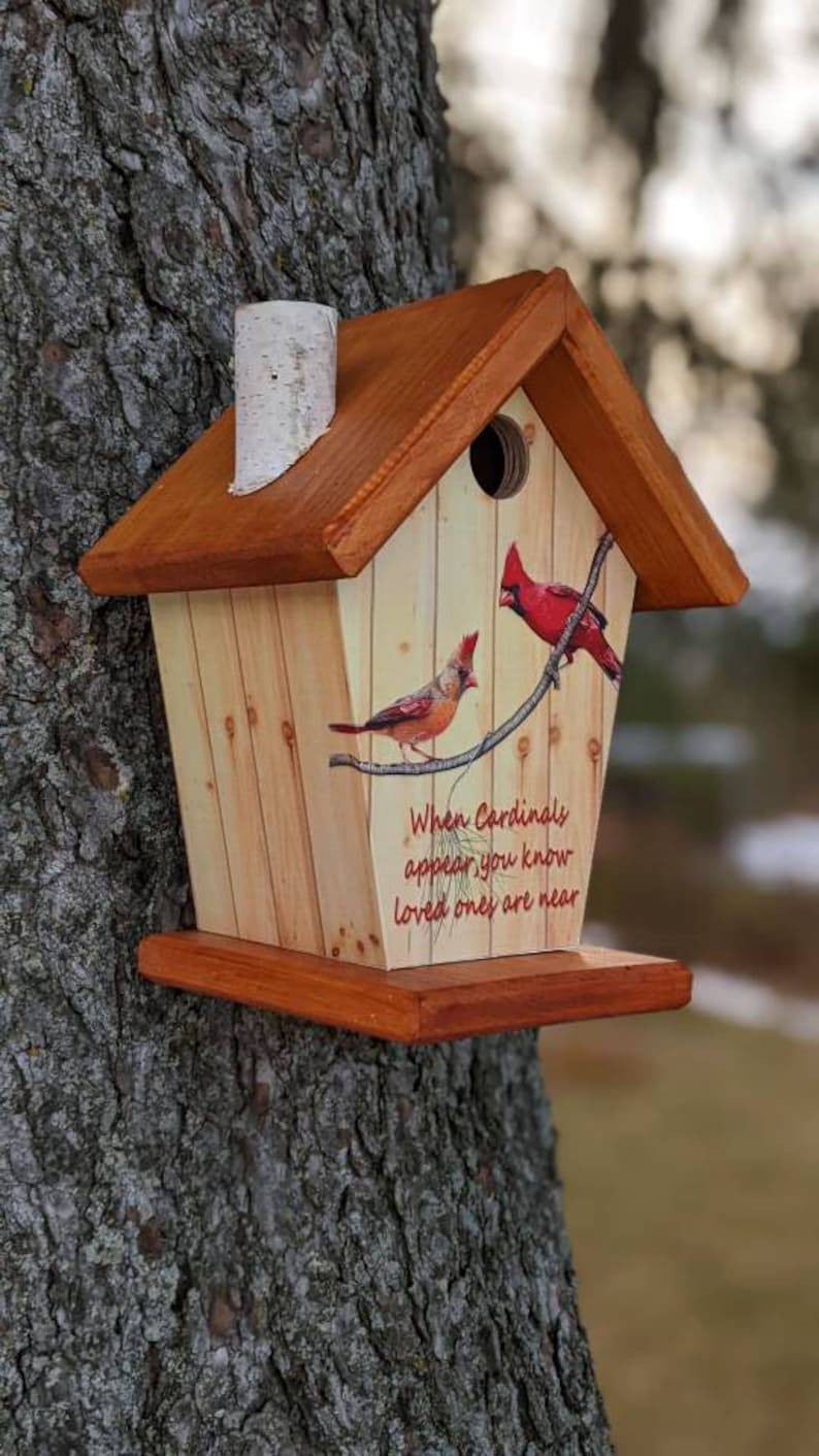 May include: Wooden birdhouse with a pitched roof and a small chimney. The birdhouse is decorated with images of red cardinals perched on a branch, with the text "When Cardinals appear you know loved ones are near."