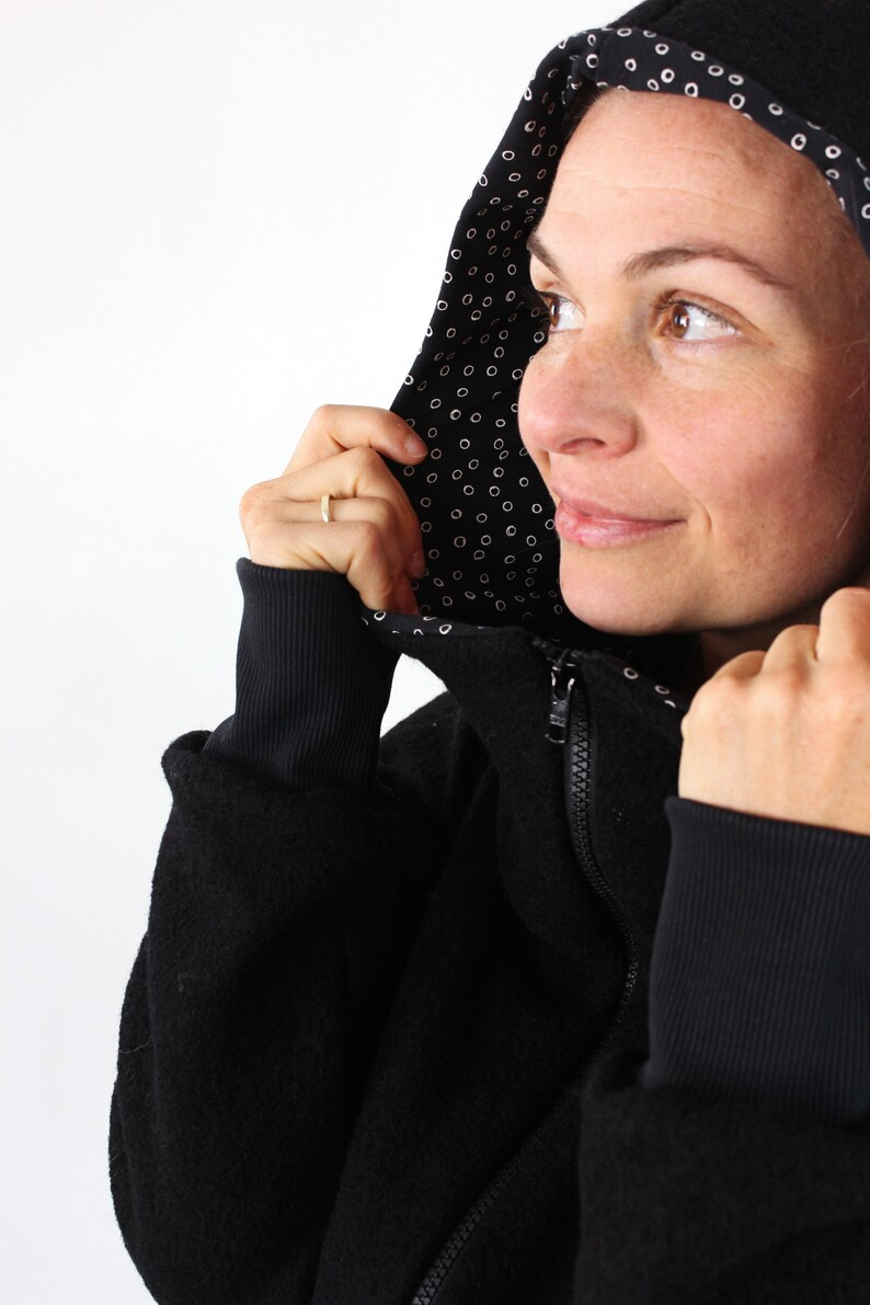 May include: A black hooded sweatshirt with a white polka dot lining. The hood is pulled up and the person is looking to the right.