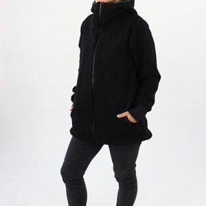 May include: A black fleece jacket with a high collar and a zipper closure. The jacket has a relaxed fit and is worn by a person with black jeans and a black headband.