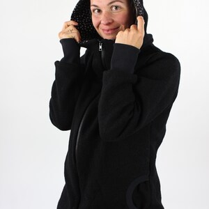 May include: A black hooded jacket with a zipper closure and a black and white patterned lining. The jacket has a large pocket on the left side.