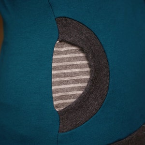 Op de afbeelding: Tealblauw shirt met een grijze zak. De zak heeft een gestreepte voering.