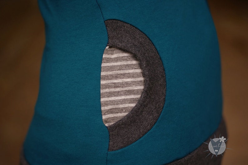 Op de afbeelding: Tealblauw shirt met een grijze zak. De zak heeft een gestreepte voering.