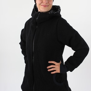 May include: A black hooded jacket with a zipper closure and a small pocket on the left side. The jacket has a black and white patterned lining around the hood.