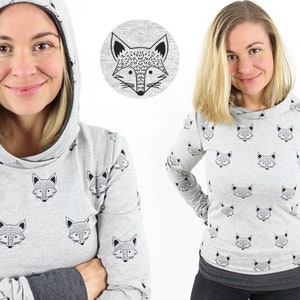May include: Two women wearing grey long-sleeved shirts with a fox print. One shirt has a hood and the other has a crew neck. Both shirts have black fox faces printed on them.