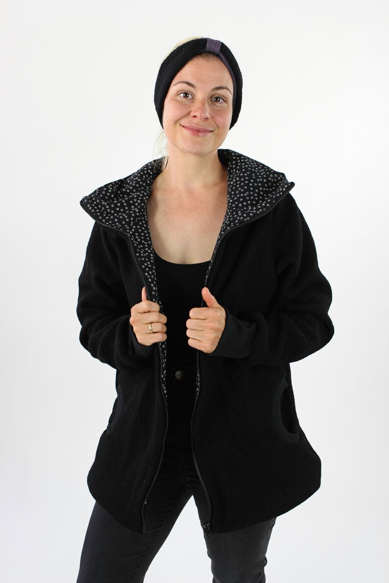 May include: A black fleece jacket with a zipper closure and a hood. The jacket has a white and black patterned lining. The model is wearing black jeans and a black headband.