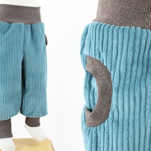 Pode incluir: Calça de veludo cotelê azul-turquesa com cintura e punhos de malha canelada marrom. A calça tem um design único com círculos de tecido marrom na frente e atrás.