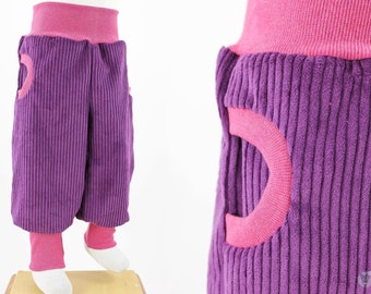 Purple romper trousers made of wide corduroy with pockets and pink mottled waxed cuffs, fit well beyond the basic size