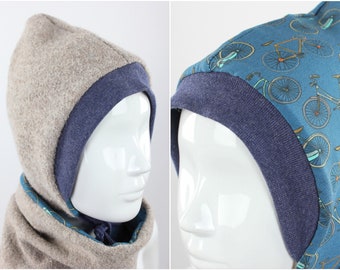May include: A hooded scarf in two sections. The outer layer is a light tan wool-like material, and the inner layer is a blue fabric. The hood's interior features a bicycle pattern on a teal background. The trim is a solid navy blue.