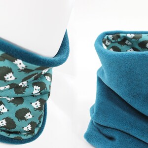 Puede incluir: Un cuello de lana de color azul turquesa con un forro de estampado de erizo. El cuello es reversible, con un lado de color azul turquesa sólido y un lado con un estampado de erizo.