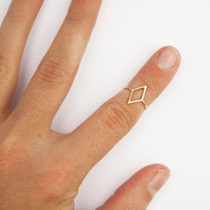 Very thin wire creating the outline of a diamond shape with thin wire as the ring band. Shown in gold tone with a light hammered finish worn as a midi ring on the top of a pointer finger.