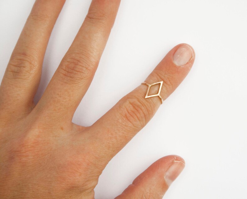 Very thin wire creating the outline of a diamond shape with thin wire as the ring band. Shown in gold tone with a light hammered finish worn as a midi ring on the top of a pointer finger.