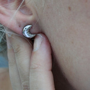 Silver crescent moon earring being shown worn on a models ear.