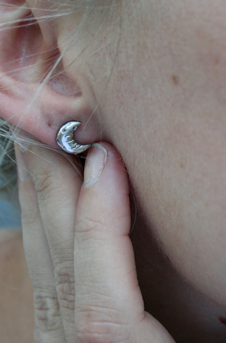 Silver crescent moon earring being shown worn on a models ear.