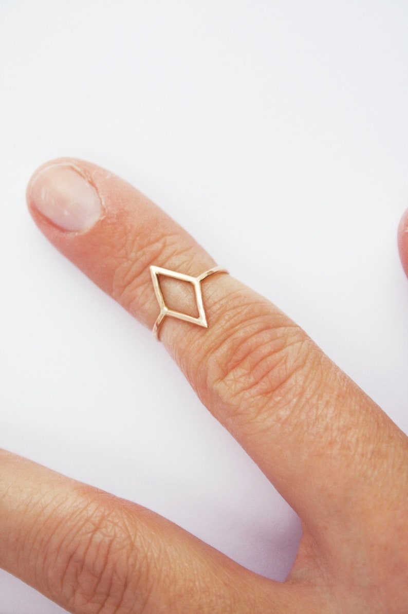 Very thin wire creating the outline of a diamond shape with thin wire as the ring band. Shown in gold tone with a light hammered finish worn as a midi ring on the top of a pointer finger.