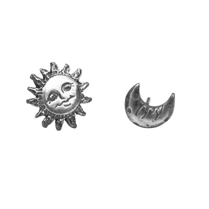 Silver mismatching Sun and Moon Earrings. On the left is the sun with textured rays and a smiling face carved in the center. The crescent moon on the right has sleepy eyes and a smile on his face.