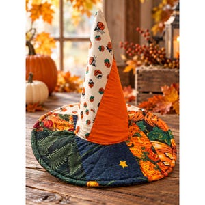May include: A quilted fabric witch hat featuring a patchwork design with various patterns including orange pumpkins, green ferns, and small yellow stars. The cone-shaped crown is divided into sections of cream fabric with pumpkin prints and solid orange fabric.