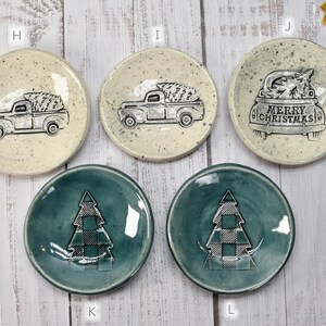 May include: A collection of small, round ceramic plates with Christmas-themed designs. Some plates feature a truck carrying a Christmas tree, while others display a plaid Christmas tree. The plates are in various colors.