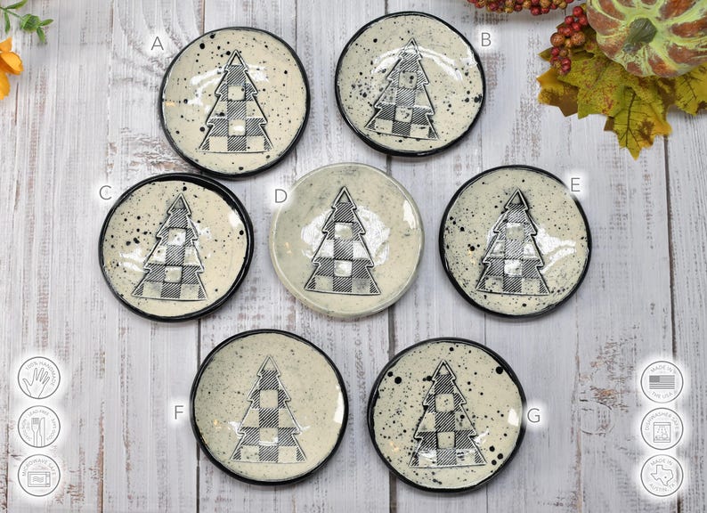 May include: A collection of seven small, round ceramic dishes. Each dish features a black and white checkered Christmas tree design in the center. The dishes have a speckled, off-white background and black rims.