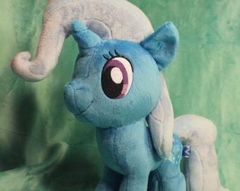 May include: A plush toy of a blue unicorn with a white mane and tail. The unicorn has a purple eye and a white horn.