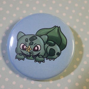 Peut inclure: Un bouton bleu avec une image de dessin animé d'un Bulbasaur Pokemon vert tenant une fleur jaune.