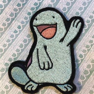 May include: A blue and black embroidered patch of a cartoon character with a big smile and one arm raised in a wave. The character has a large, round head and a small, round body.