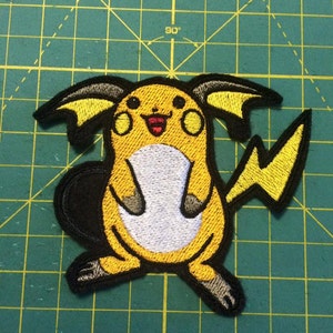 May include: Yellow and black embroidered patch of a cartoon Pikachu with a white belly and a red mouth.