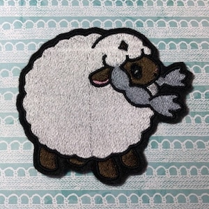 May include: White embroidered sheep with brown legs and a gray face. The sheep is holding a gray and white scarf in its mouth.