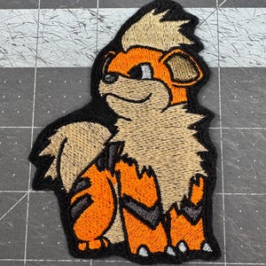 Peut inclure: Écusson brodé représentant un personnage de dessin animé ressemblant à un chien, avec des détails orange, beige et noirs. Le patch a une bordure noire et est conçu pour être appliqué sur du tissu. Le personnage a une expression amicale.