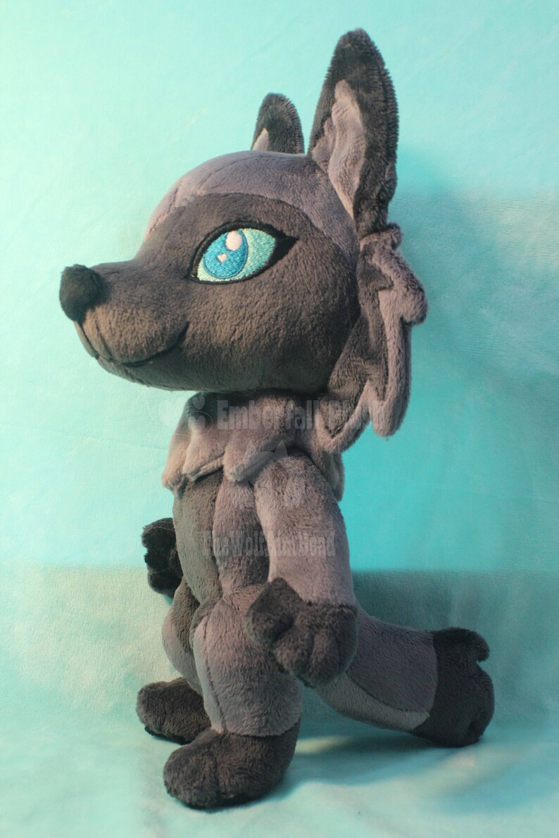 May include: A gray plush wolf with blue eyes and a white nose. The wolf is standing on a light blue surface.