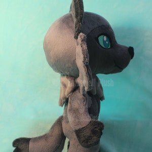 May include: A gray plush wolf with blue eyes. The wolf is standing on a light blue surface.