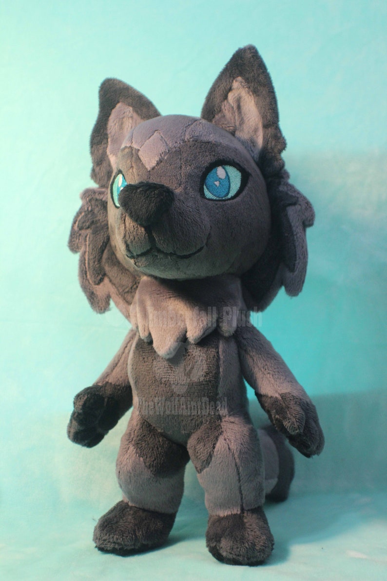 May include: A gray plush wolf with blue eyes. The wolf is standing on a light blue surface.