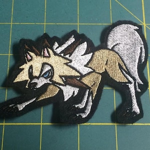 May include: Embroidered patch of a white and brown wolf with blue eyes, in a snarling pose. The wolf is on a black background.