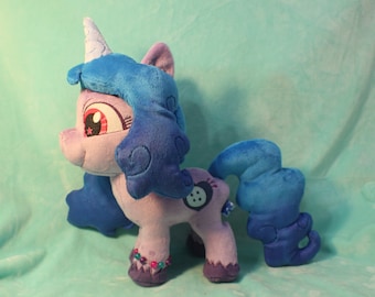 May include: Purple and blue plush toy pony with a blue mane and tail. The pony has a pink nose, red eyes, and a white horn with a star on it. The pony is wearing a purple and blue bracelet with beads.