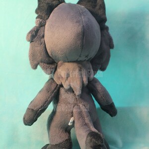 May include: A gray plush toy in the shape of a wolf or fox. The toy is standing on a light blue surface. The toy has a long tail and large ears.