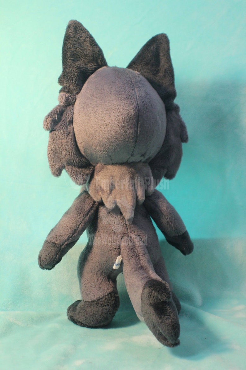 May include: A gray plush toy in the shape of a wolf or fox. The toy is standing on a light blue surface. The toy has a long tail and large ears.