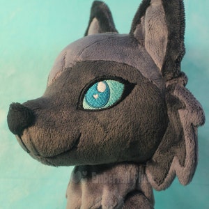 May include: A gray plush wolf with blue eyes and a fluffy tail. The wolf is looking to the right and has a slight smile.