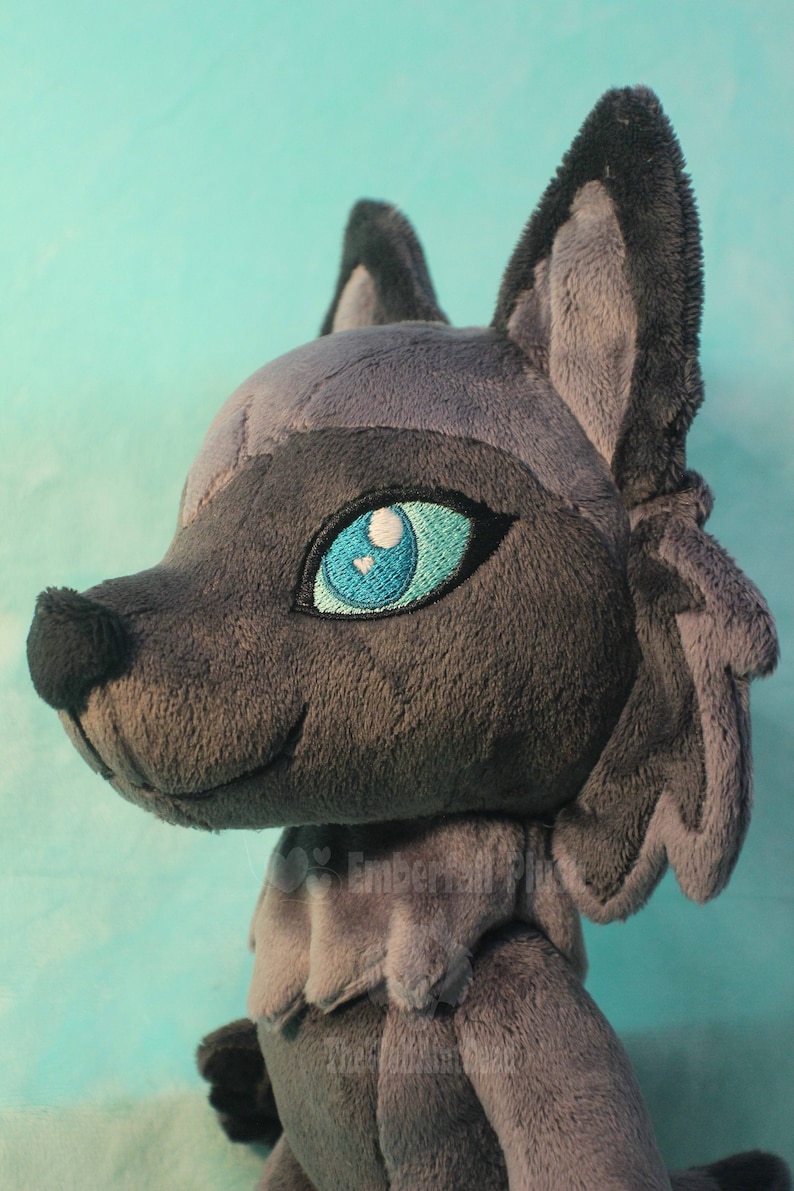 May include: A gray plush wolf with blue eyes and a fluffy tail. The wolf is looking to the right and has a slight smile.