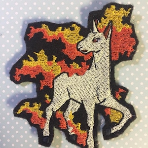 May include: Embroidered iron-on patch featuring a white unicorn with a red eye, standing in a black, red, and gold flame design.