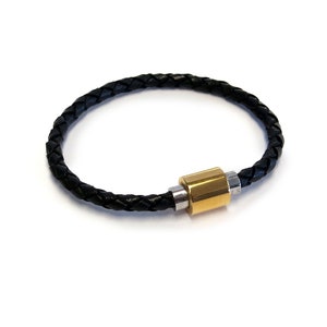 May include: A black leather bracelet with a gold and silver magnetic clasp. The bracelet is braided and has a simple design.