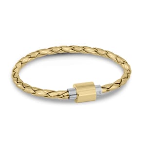 May include: A gold-toned braided bracelet featuring a cylindrical clasp mechanism. The clasp consists of a central gold-colored barrel flanked by two silver-toned metal rings, with the letters LS visible on the side of one silver ring.