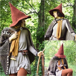 May include: A woman wearing a brown pointed hat with a brown and white patterned cape. She is holding a staff in her hand and is standing in a forest.