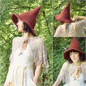 May include: A woman wearing a brown pointed witch hat with a wide brim and a crocheted shawl. She is standing in a forest setting.