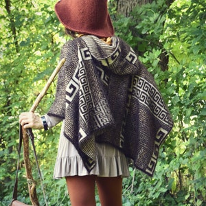 May include: A person wearing a brown hooded knitted poncho with a geometric pattern, a brown pointed hat, and brown pants. The person is holding a wooden walking stick with a brown leather bag attached.
