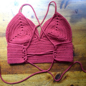 May include: A red crocheted halter top with a criss-cross tie in the back and tassels on the ends of the ties.