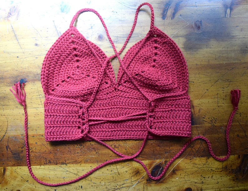 May include: A red crocheted halter top with a criss-cross tie in the back and tassels on the ends of the ties.