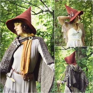 May include: A woman wearing a brown knitted hat with a pointed top and a brown and white patterned cape. She is standing in a forest setting.